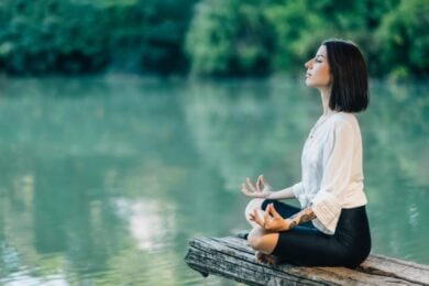 Frau sitzt am See und meditiert